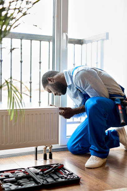 Man in workwear overalls using tools while installing or repairing heating radiator in room. plumber installing heating system in apartment. radiator installation, plumbing works and home renovation